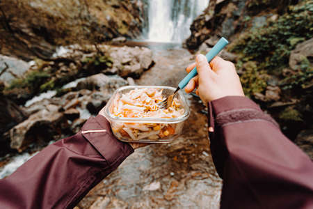 A horizontal shot of a point of view shot of a female hiker eating in front of a waterfallの写真素材