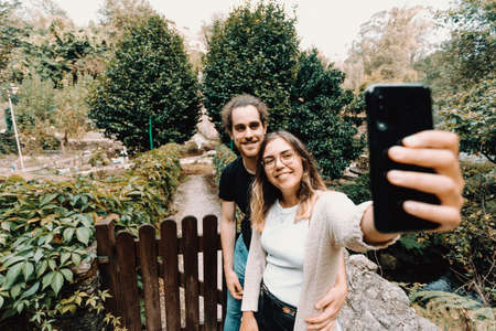 A young and smiling couple taking a selfie in front of a beautiful rural houseの写真素材