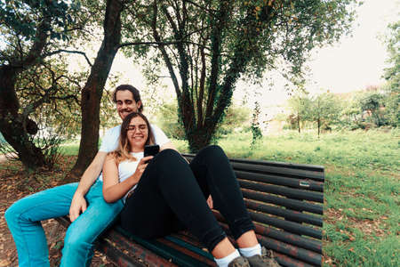 A young couple looking at the smart phone in a bench on the park while smilingの写真素材