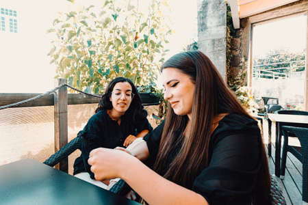 A young woman showing something on the phone making a friend laugh in the barの写真素材