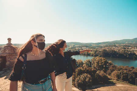 Two women look the panorama while one explains something, both using masksの写真素材