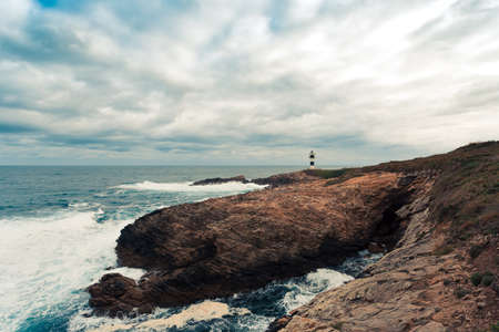 A wild lighthouse in the coast of the north of Spain with giant rocks an wild waves crashing with copy spaceの写真素材