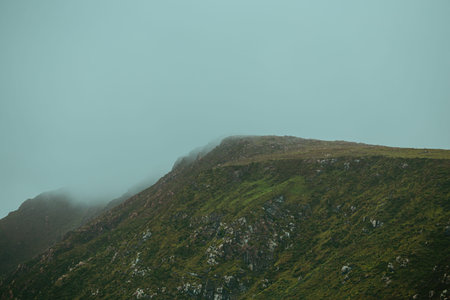 A close up of a mountain with green grass all over it during a foggy day with mist all over it with...