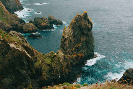 The cliffs and giant stones in europe with the wild ocean breaking against it on green and brown tonesの写真素材