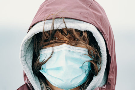 A close up of a woman face with the mask put on and the hair flying by the wind while wearing hiking...