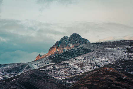 A panoramic view of a giant rock in the snowy mountain with the sunset reflecting on itの写真素材