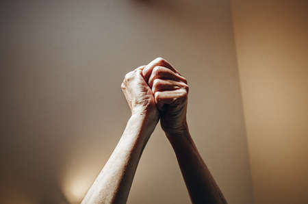 Two old woman hands rised grabbing each other on pastel tones with lights surroundingの写真素材