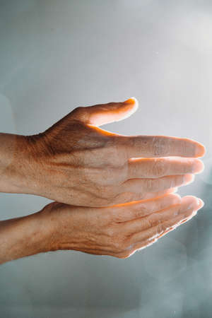 Two old hands asking for something while the light reflects in the handsの写真素材