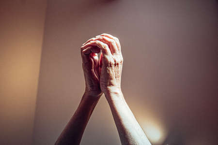Two old woman hands raised in religious position asking for something in pink tones with bright lightsの写真素材