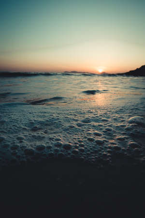 A super close up of the bubbles in the tide of the beach during a sunsetの写真素材