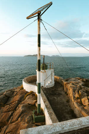 A green and white lighthouse in front of the ocean and an island during a summer dayの写真素材