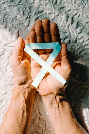 A close up of two old hands grabbing a blue ribbon for the international diabetes dayの写真素材