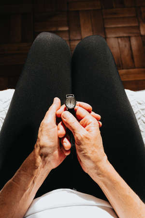 A close up of two old hands grabbing a watch and looking the time while sitting on his bedの写真素材