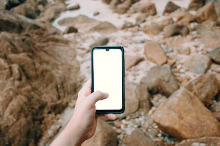 A young male hand grabbing a phone with copy space with a background of rocks in the beachの写真素材