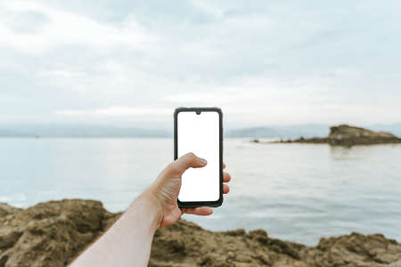 A young male hand grabbing a phone with copy space with the sea as the backgroundの写真素材