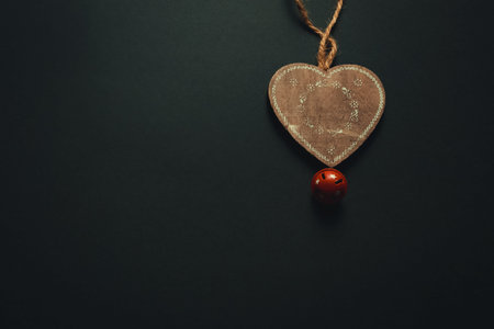 A christmas flat lay with a wooden heart and a jingle bell over a dark background with copy space