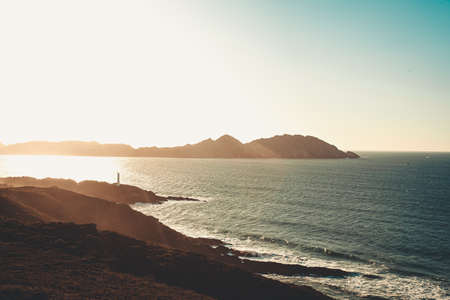A super bright sunset over a lighthouse in front of an island on the spanish coast during the autumn with copy spaceの写真素材