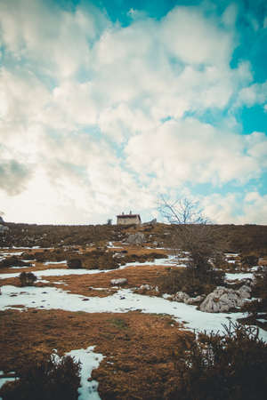 A minimalistic shot of a house on the top of a mountain with a lot of copy space and a cloudy sky and snowの写真素材