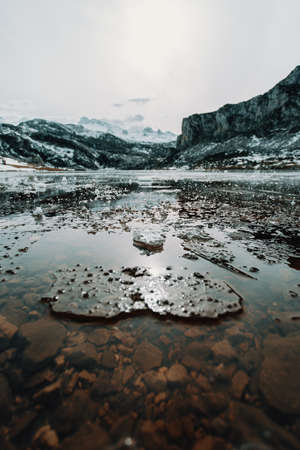 Some frozen water and pieces of ice in a frozen lake in the middle of the mountains during winterの写真素材
