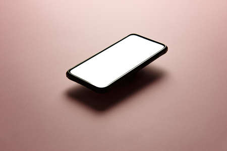 A minimalistic mock up flat image design of a mobile phone with copy space and white scree to write over it over a flat pastel pink backgroundの写真素材
