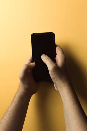 A top view of two young hands using a mobile phone with copy space and a black screen over a pink yellow backgroundの写真素材