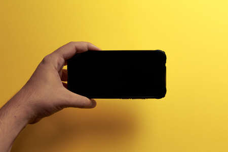 A young hand showing something on a phone screen with copy space over a yellow background in horizontalの写真素材