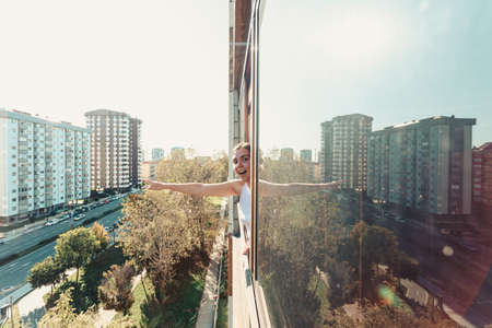 A surprised young woman pointing out something and looking to camera while on a window with the city as the backgroundの写真素材