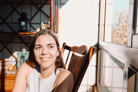 A young on vintage clothes woman sitting near a window with a bright day and smiling with copy space and colorfulの写真素材