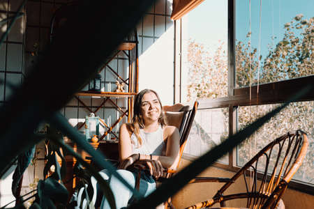 A young on vintage clothes woman sitting near a window with a bright day and smiling with copy space and colorfulの写真素材