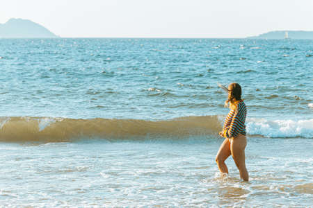 A young woman walking on the sea in the beach during a bright day with a sweater put on and copy spaceの写真素材