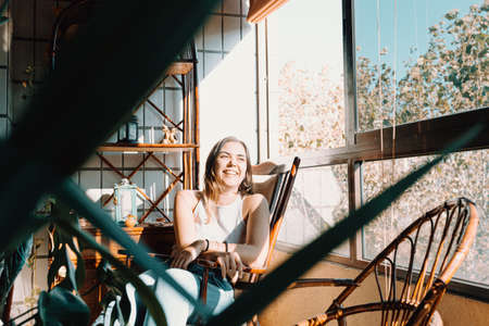 A young on vintage clothes woman sitting near a window with a bright day and smiling with copy space and colorfulの写真素材