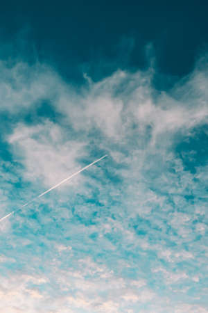 A plane flying on the sky between the clouds in a minimalistic image with a saturated blue colorの写真素材
