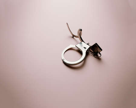 A pair of metallic handcuffs over a flat and bright pastel pink backgroundの写真素材