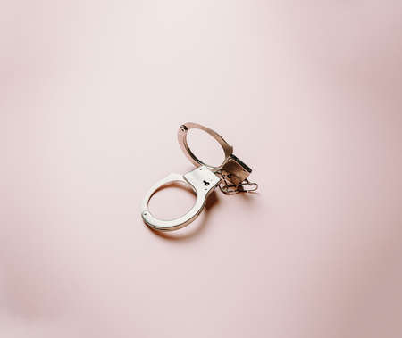 A pair of metallic handcuffs over a flat and bright pastel pink backgroundの写真素材