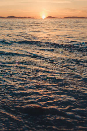 A vertical image of a tide on the beach over the sand during a colorful sunset with the islands as the background and copy spaceの写真素材