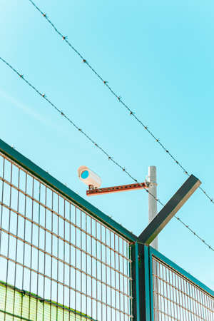 A minimalistic and colorful shot of a surveillance camera with a wall and a barbed wireの写真素材