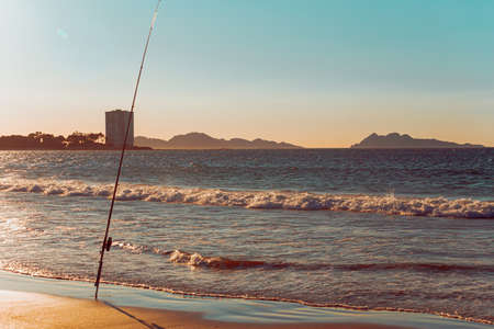 A fishing rod in a beach in front of a massive building during a sunset in Spainの写真素材