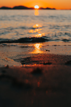 A massive sunset over the islands reflecting over the ocean with the sun and the tides on the beach over the sand during spring, on colorful tones with copy spaceの写真素材