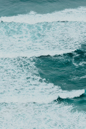 Aerial view of the ocean with the waves and re rocks during a bright day, relaxing scene on blue...