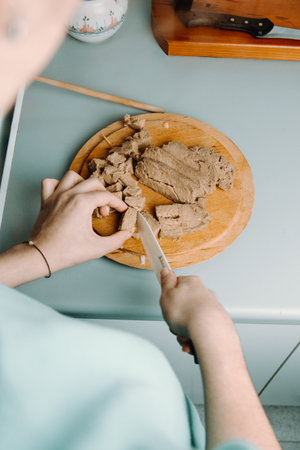 A woman cutting some tofu over a wooden round plate with a knife while cookingの写真素材
