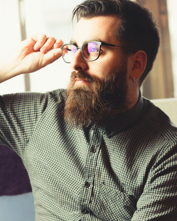 A young hipster male holding his blue light glasses while looking away to camera with a smiling faceの写真素材