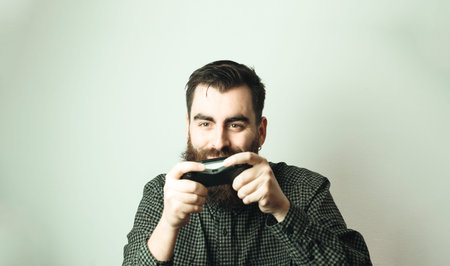 A young hipster man with a white background holding a console pad while smiling