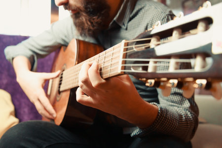 A close up of the hands of a bearded man playing the spanish guitar during a bright dayの写真素材