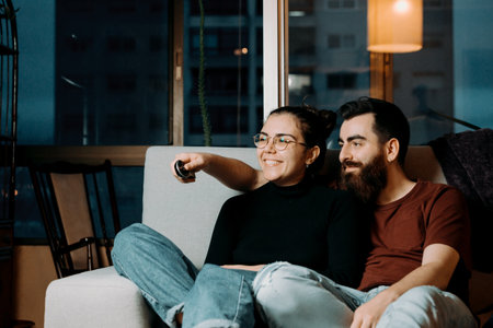 A couple on the couch looking away from camera to the tv while holding the tv remote and smilingの写真素材