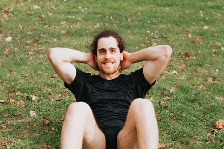 Close up of a young man training at the park over the grass doing crunches while smiling to cameraの写真素材