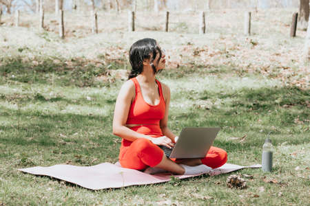 Young woman in fitness clothes relaxing on his laptop at the park over over a yoga mat with copy spaceの写真素材