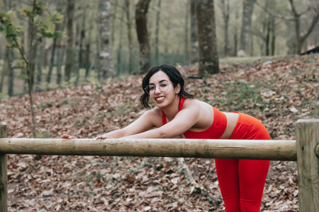 Young woman in fitness clothes stretching his body at the park while smiling to camera