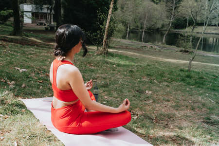 Young woman in fitness clothes doing yoga exercises over a yoga mat at the park during a sunny dayの写真素材