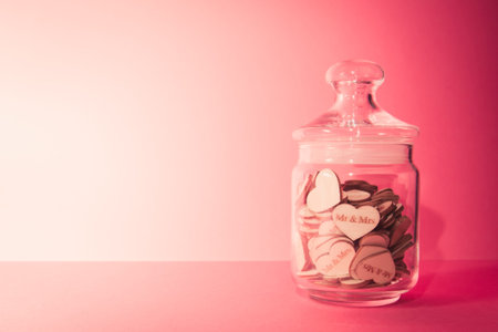 Crystal white bottle with wooden hearts in it over a pastel pink background with copy spaceの写真素材