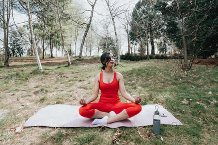 Young woman in fitness clothes doing yoga exercises over a yoga mat at the park during a sunny dayの写真素材